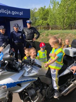Chłopiec siedzący na motocyklu i kilkoro dzieci i policjant stojący obok niego