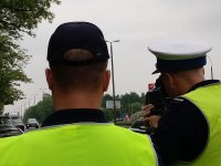 dwaj policjanci w kamizelkach odblaskowych, z których jeden z nich mierzy prędkość kierujących