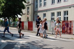 Na obrazku widoczne są policjantki przeprowadzające dzieci przez przejście dla pieszych.