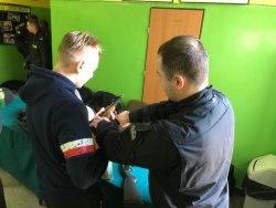 Policjant pokazuje chłopakowi jak obsługiwać broń długą.