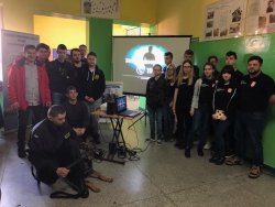 Wewnątrz pomieszczenia grupa młodzieży oraz policjant z psem służbowym pozują do zdjęcia