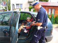 Dziecko siedzące w foteliku w samochodzie a przy pojeździe stoi policjant