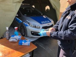 radiowóz i policjantka zakładająca jednorazowe rękawiczki a obok stolik ze środkami dezynfekującymi