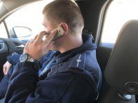 policjant siedzi w radiowozie i dzwoni z telefonu komórkowego do osoby objętej kwarantanną