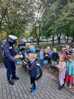 policjant ruchu drogowego rozdaje grupie dzieci elementy odblaskowe
