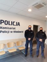 Dwaj umundurowani policjanci na tle logo Komisariatu Policji w Kłodawie