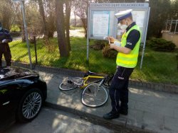 Umundurowany policjant służby drogowej, ogląda zniszczony rower leżący na ziemi.