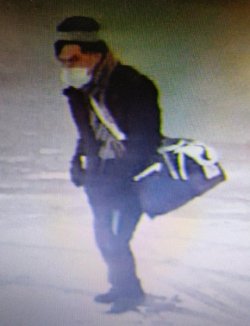 zdjęcie z monitoringu, na którym widać mężczyznę w maseczce, z torbą podróżną idącego po placu