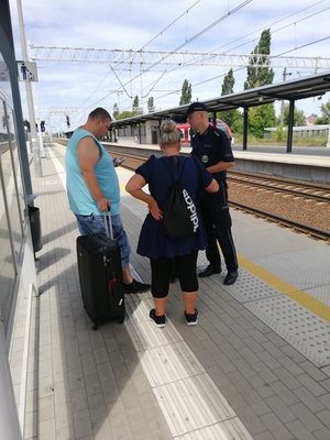 Na zdjęciu widzimy dworzec kolejowy gdzie umundurowany policjant wręcza podróżującym ulotki informacyjne odnośnie &quot;handlu ludźmi&quot;.