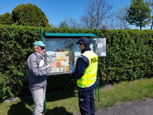 Na obrazku widzimy umundurowanego funkcjonariusza Policji w trakcie kontroli ogródków działkowych.